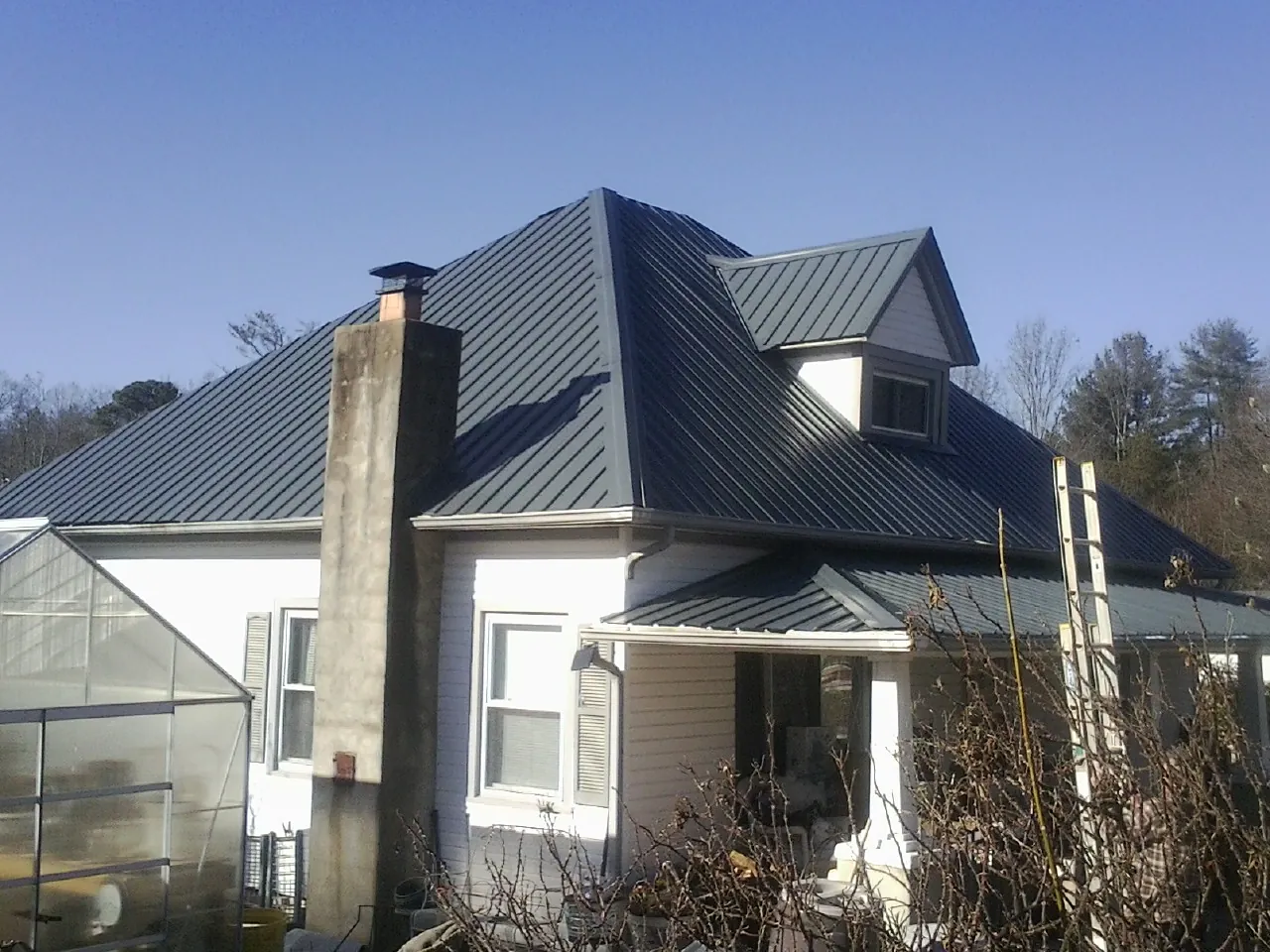 Dark blue standing seam metal roof on a white farmhouse with dormer — Slate & Tile Roof Repair by Roofing Brothers in Emerson