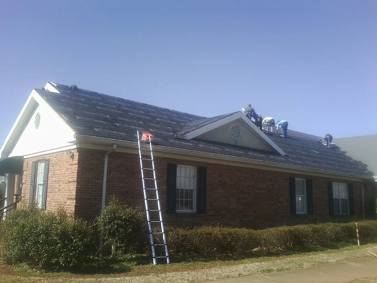 Crew tearing shingles off a brick ranch roof with a ladder set — Metal Roof Repair work by our crew in Emerson