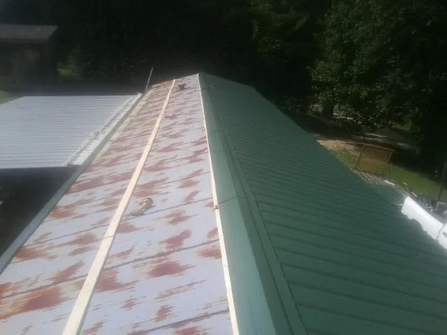 Old rusted panels beside newly installed green metal roofing — Wind Damage Roof Repair by Roofing Brothers in Emerson