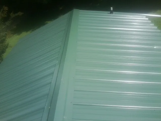 New green metal panels meeting at the ridge of a roof — Flat Roof Repair work by our crew in Emerson