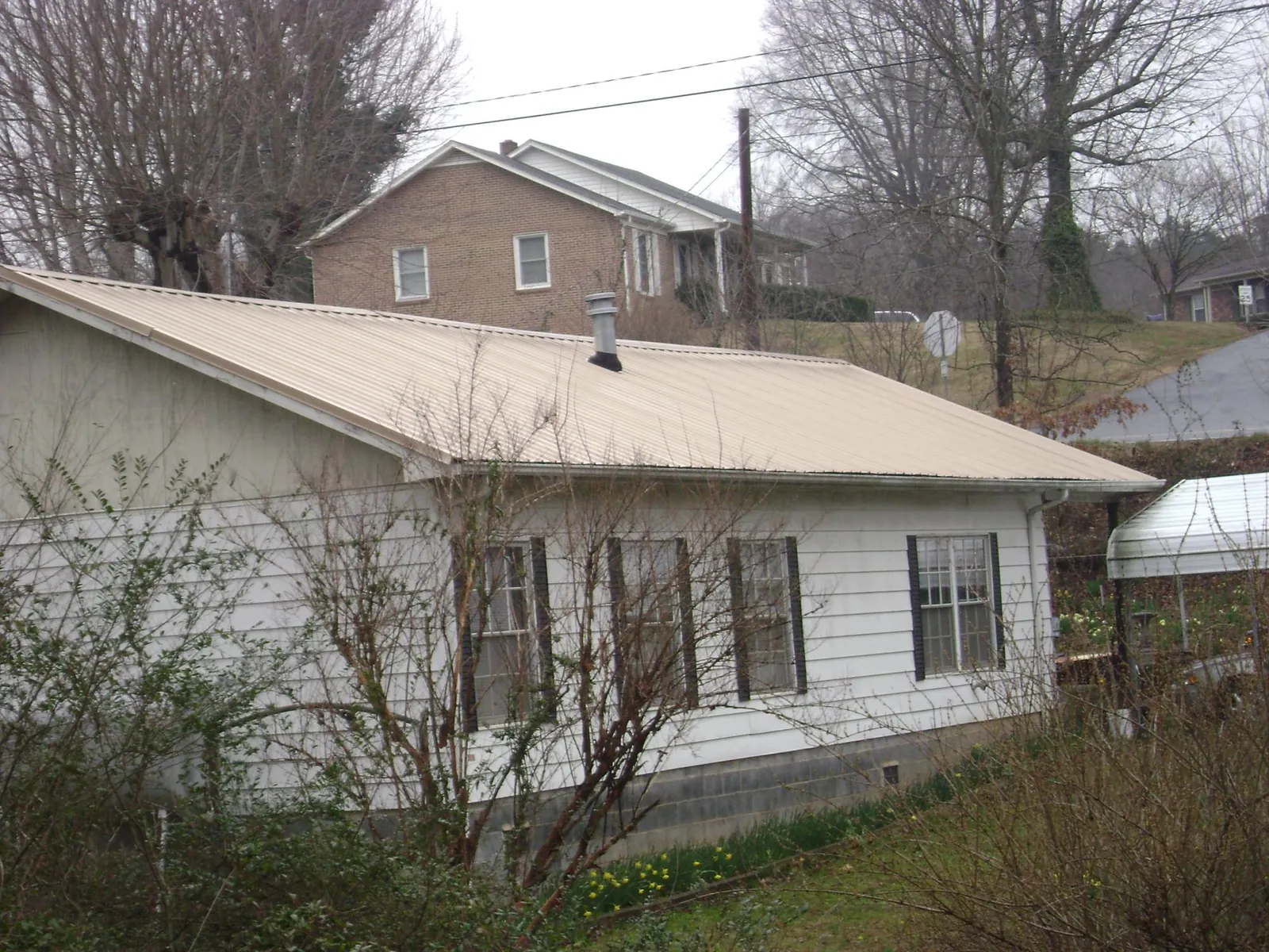 Tan metal roof on a white sided house set into a hillside — Commercial Roofing by Roofing Brothers in Emerson